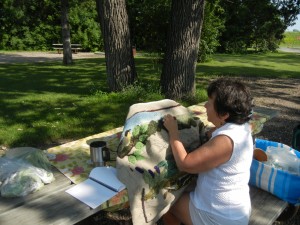 Amy rug hooking in the dappled shade of our campsite's big oak tree