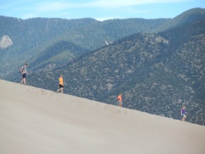 a family hiking down one of the dunes, with the Sangre de Christo Mountains in the background